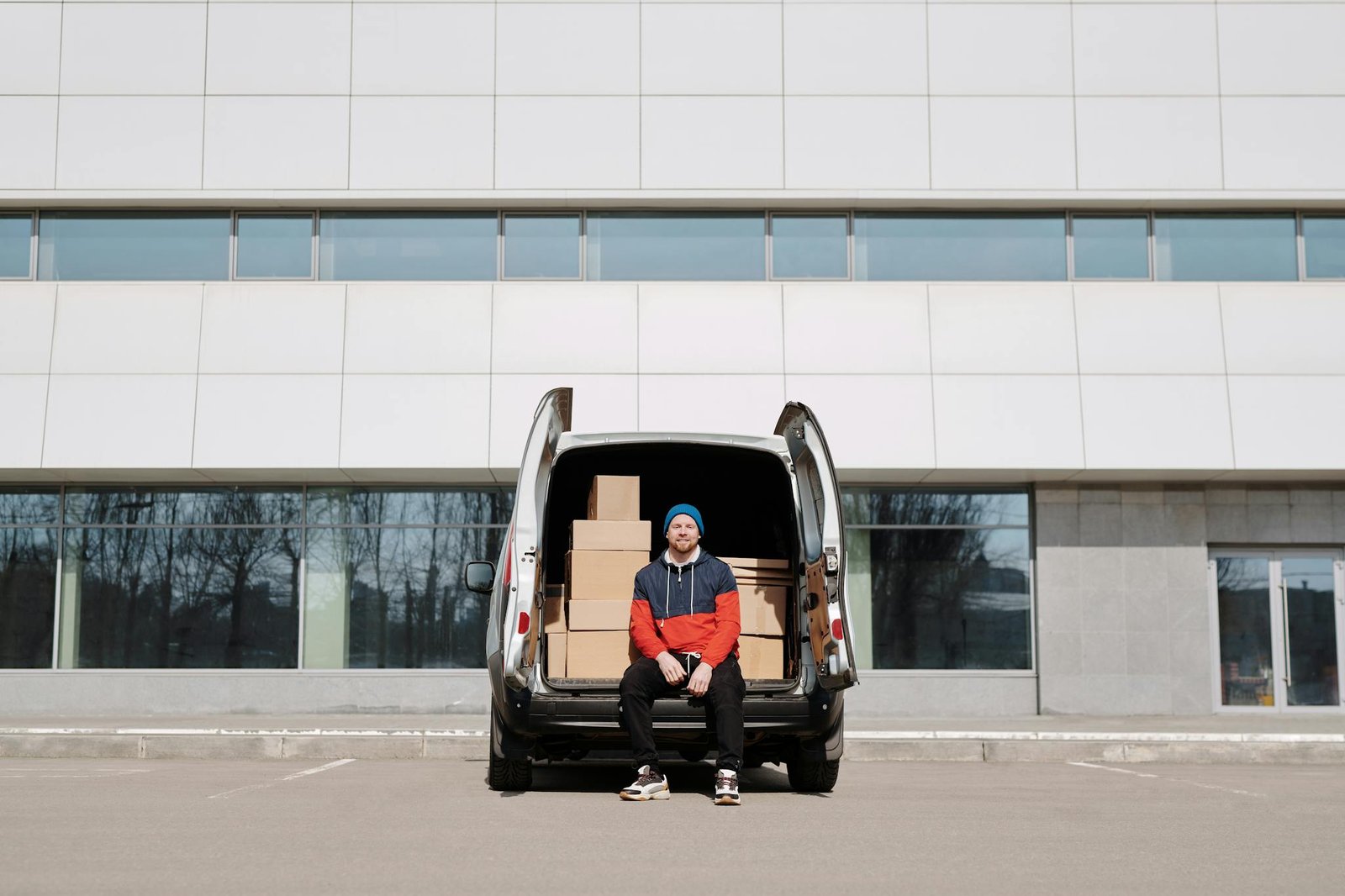 Man in a colorful jacket sitting by a van with boxes in an urban setting.
